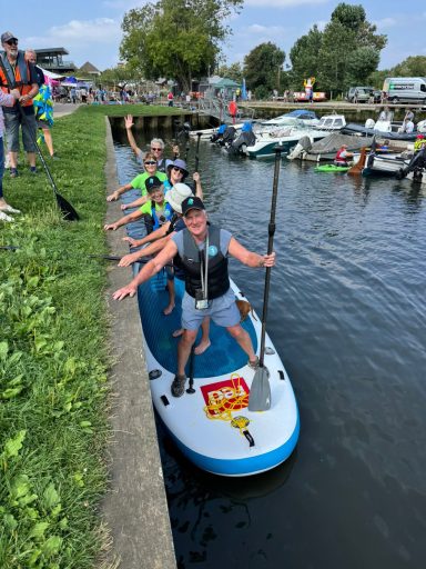 6 people on a large paddle board holding onto the side of the river.