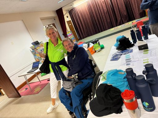 Two people, one in a wheelchair in meeting hall smiling at the camera in. Hengsitbury Head tops