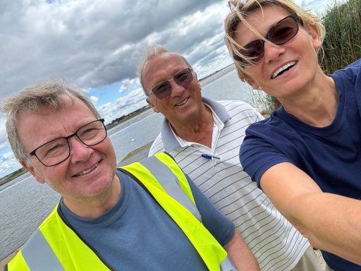 3 people smiling at the camera outside by a river
